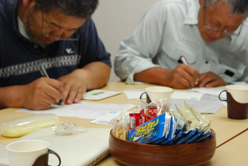 イメージキャラクター「メピカリ」が描かれたメヒカリクッキーがさりげなく。奥で作業するのは、佐藤三栄さん（右）と谷平浩さん