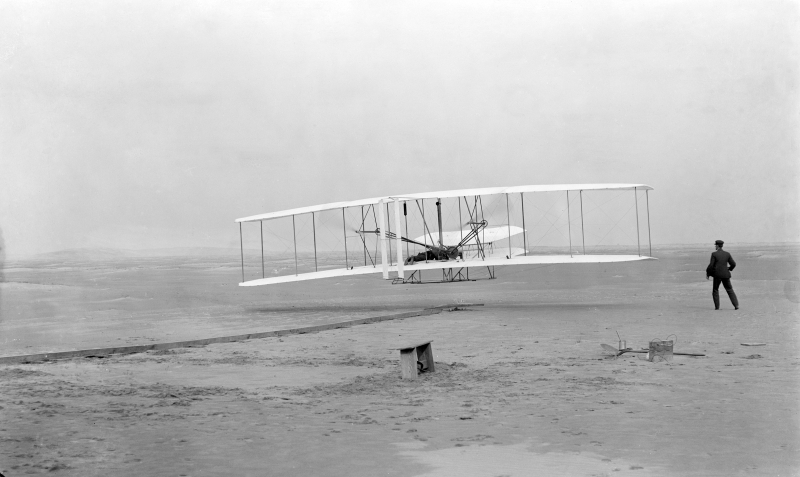 ノースカロライナ州キルデビルヒルズの砂丘における初飛行（1903年12月17日）。操縦者はオーヴィル。横にいるのはウィルバーで、離陸滑走の間、地面に触れないように支えていた翼端を離している。この飛行を見ていた観客はわずか5人であった。（Wikipediaより引用）