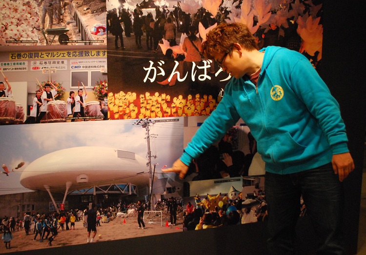 震災から2か月の2011年5月、被災した石ノ森萬画館で開催した「春のマンガッタン祭り」の写真展示を指さす大森盛太郎さん