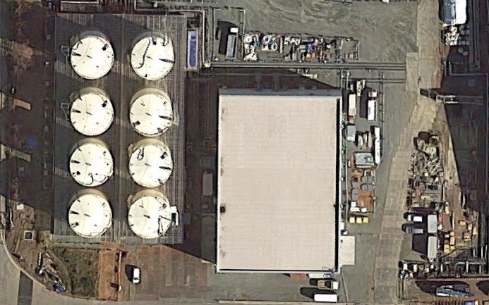 中央の建物がサブドレン他浄化設備。左のタンクが1基1000トン容量の一時貯水タンク（左上から下にA、B、C、D…の順で右下の1基は別用途：RO濃縮水処理設備）（Google Mapに加筆）