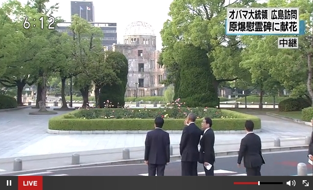 平和記念公園の北側から元安川越しに原爆ドームにのぞみ、岸田文雄外相（右）から原爆ドームと原爆の子の像についての説明を受ける。左は安倍総理；NHKの番組からキャプチャ